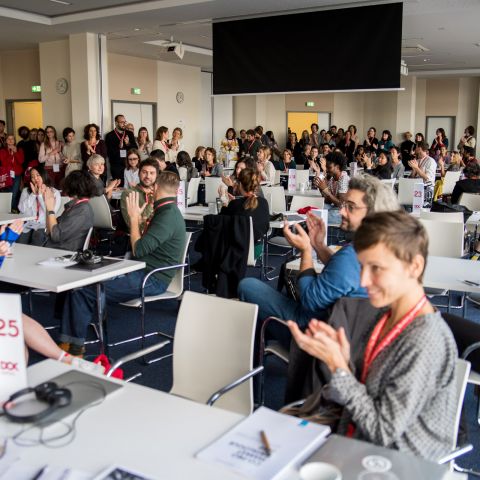 A room full of tables, chairs and applauding people