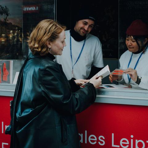 Zwei Volunteers reden mit einer Person am DOK Leipzig Infostand.