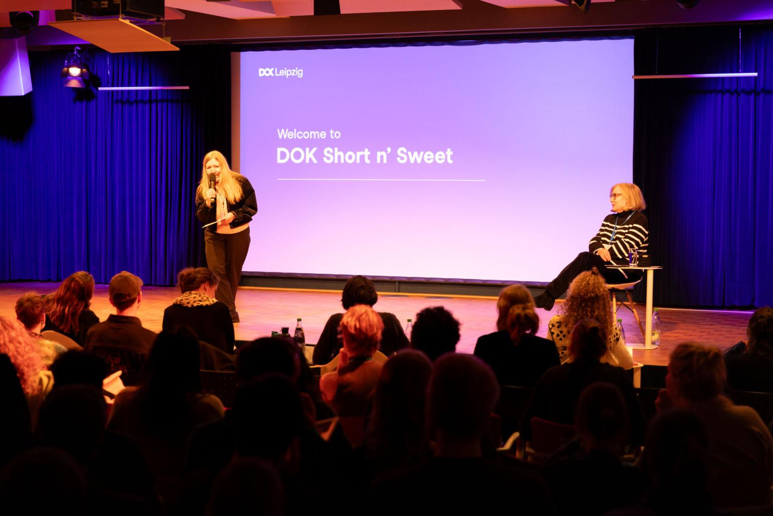 Industry Director Nadja Tennstedt welcomes the audience on stage. Behind her the text: Welcome to DOK Short n' Sweet